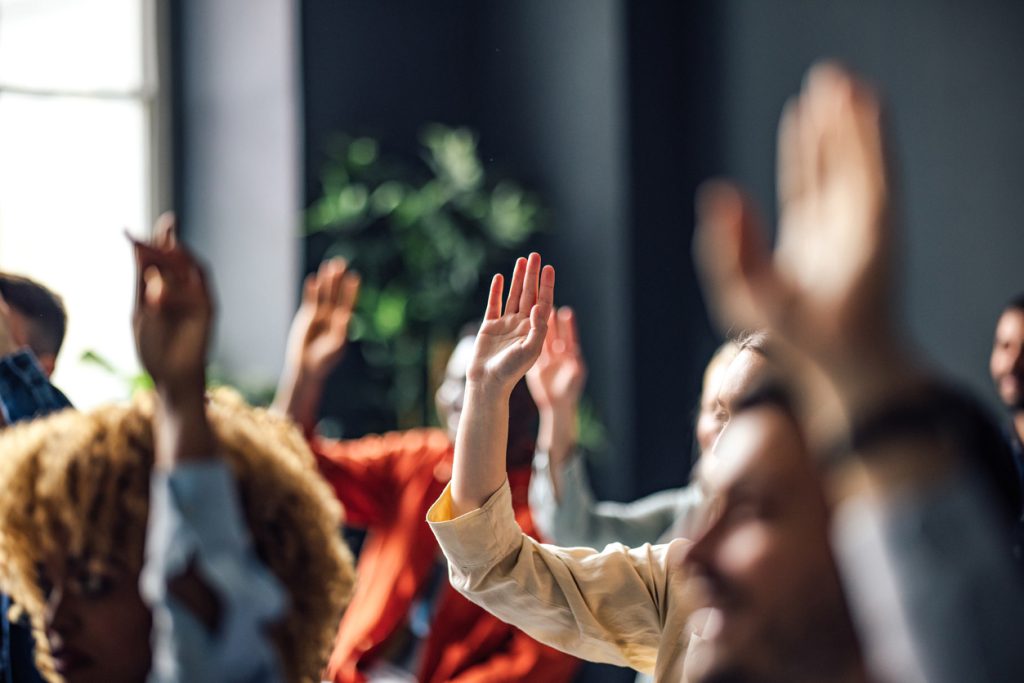 groupe de personnes levant la main pour voter dans une assemblée générale