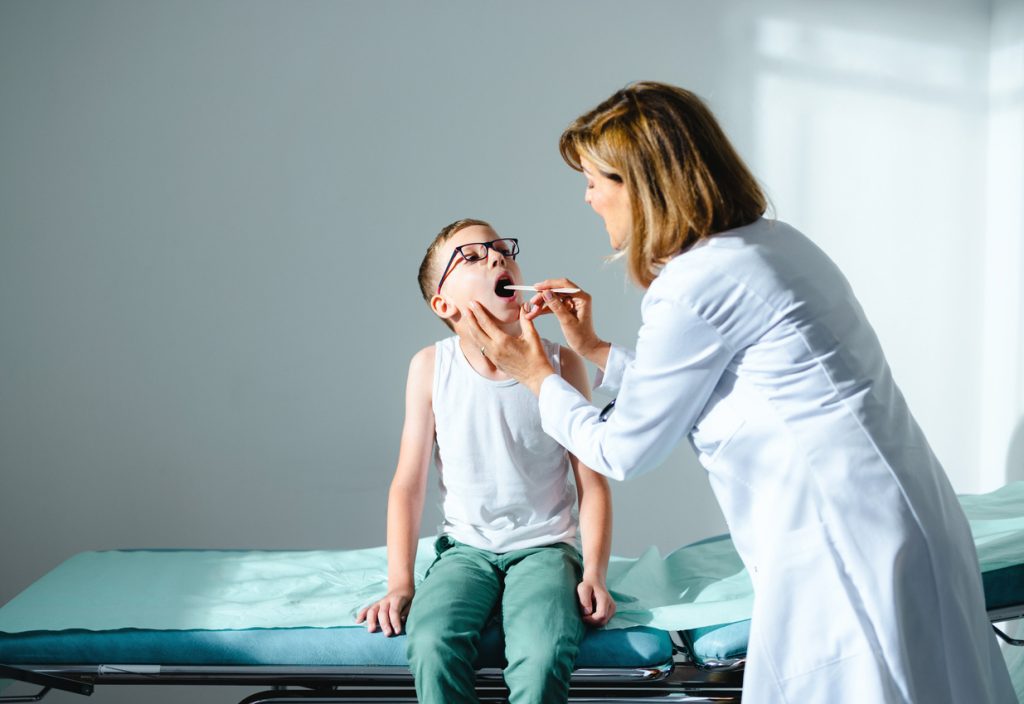 enfant se faisant ausculter la gorge chez une médecin
